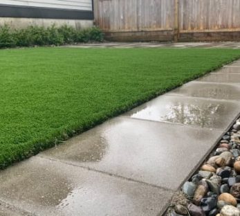 Low maintenance backyard installation of artificial lawn, concrete pavers, and river rock